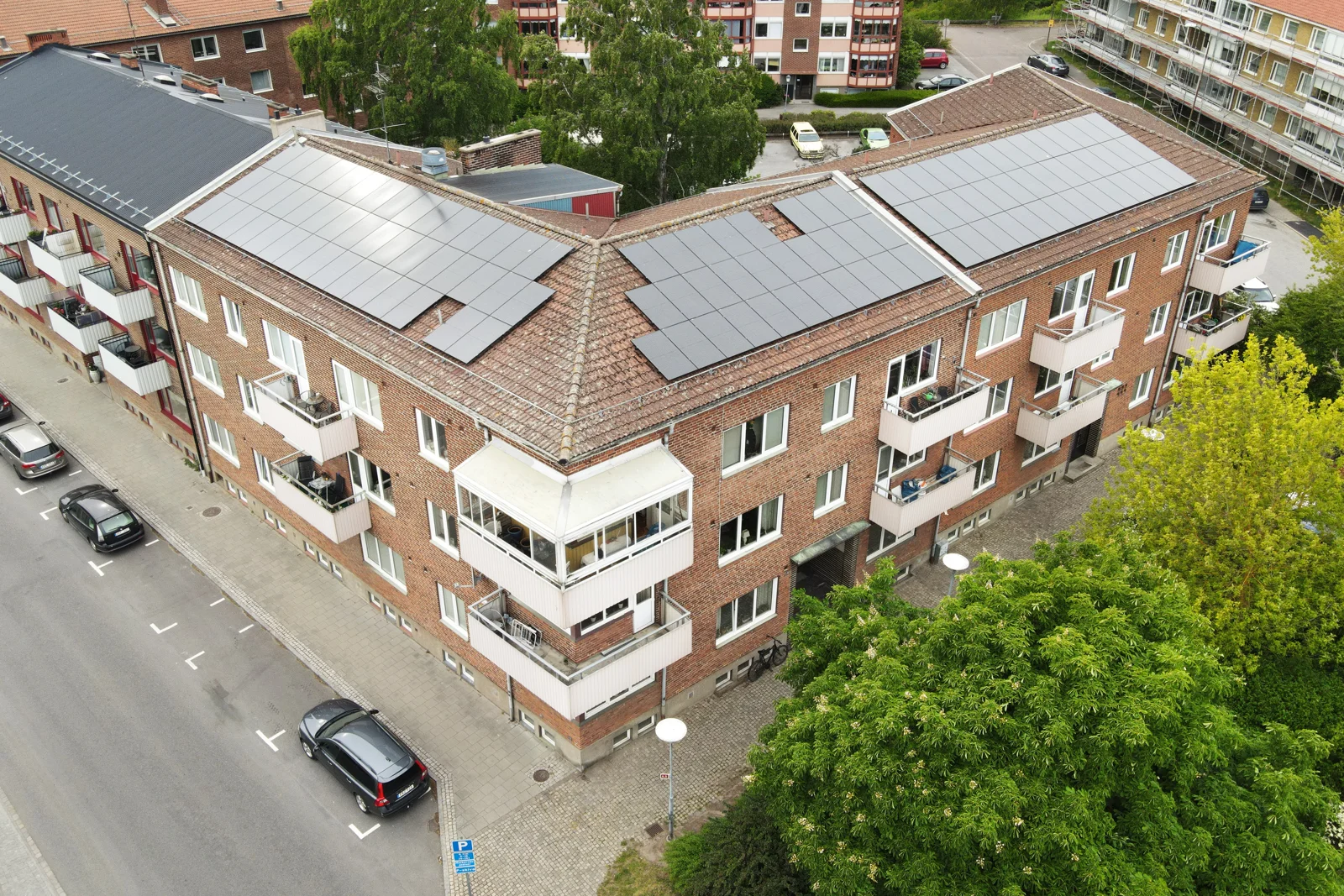 Drönarvy över ett tegelhus med balkonger, solpaneler och grönskande omgivningar